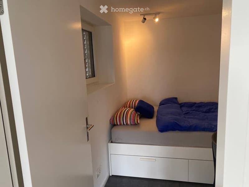 Compact bedroom with a built-in bed, colorful pillows, and storage drawers beneath the mattress.