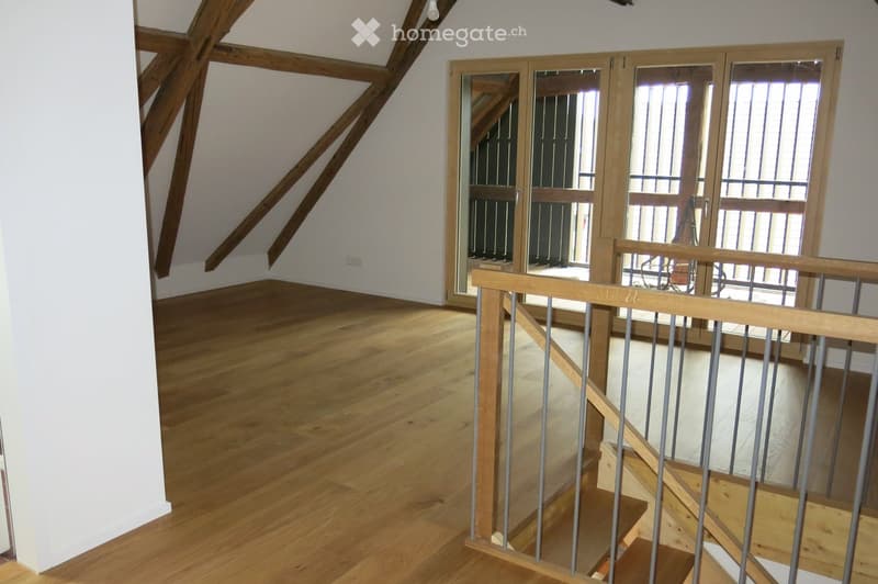 Corridor / Hallway. Spacious hallway with wooden flooring, exposed wooden beams, and a staircase leading upwards, featuring a wooden railing and glass doors at the end.