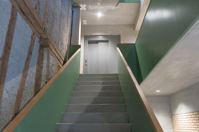 Corridor / Hallway. Modern staircase with green walls, wooden handrails, and a metal elevator door at the end.