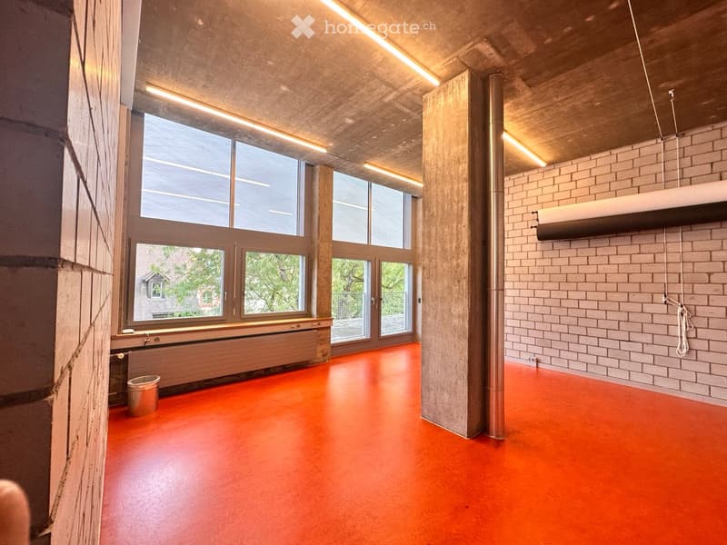 Empty room with orange floor, large windows, exposed wooden beams, and brick wall.