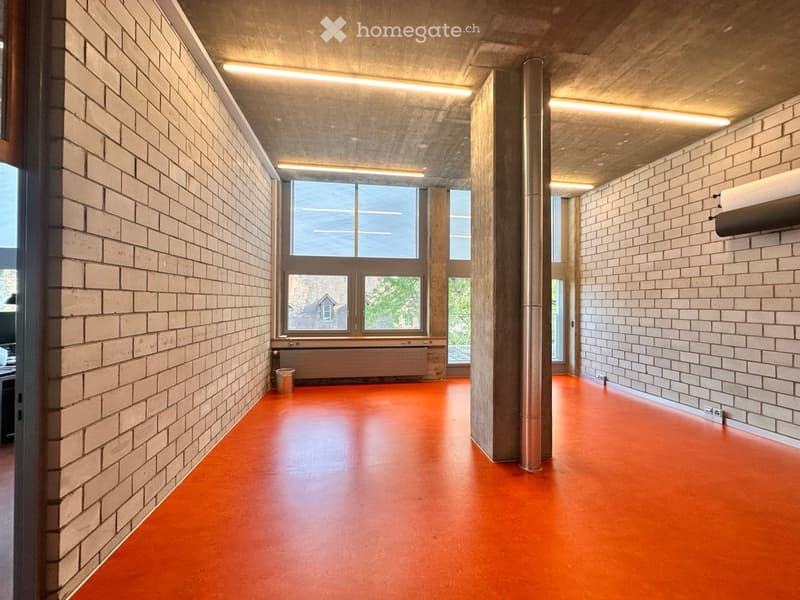 Empty hallway with exposed brick walls, orange floor, large windows, and modern lighting fixtures.
