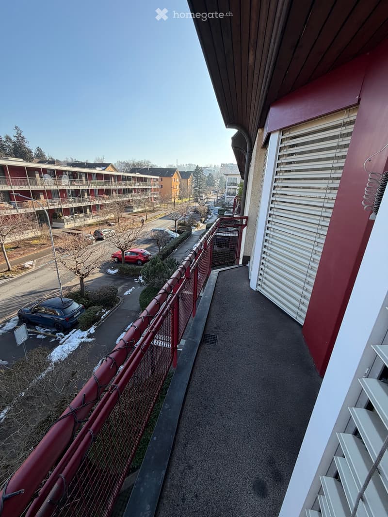 Balcony with red railing, red and white walls, window with white shutters, street view, streetlight, parked cars