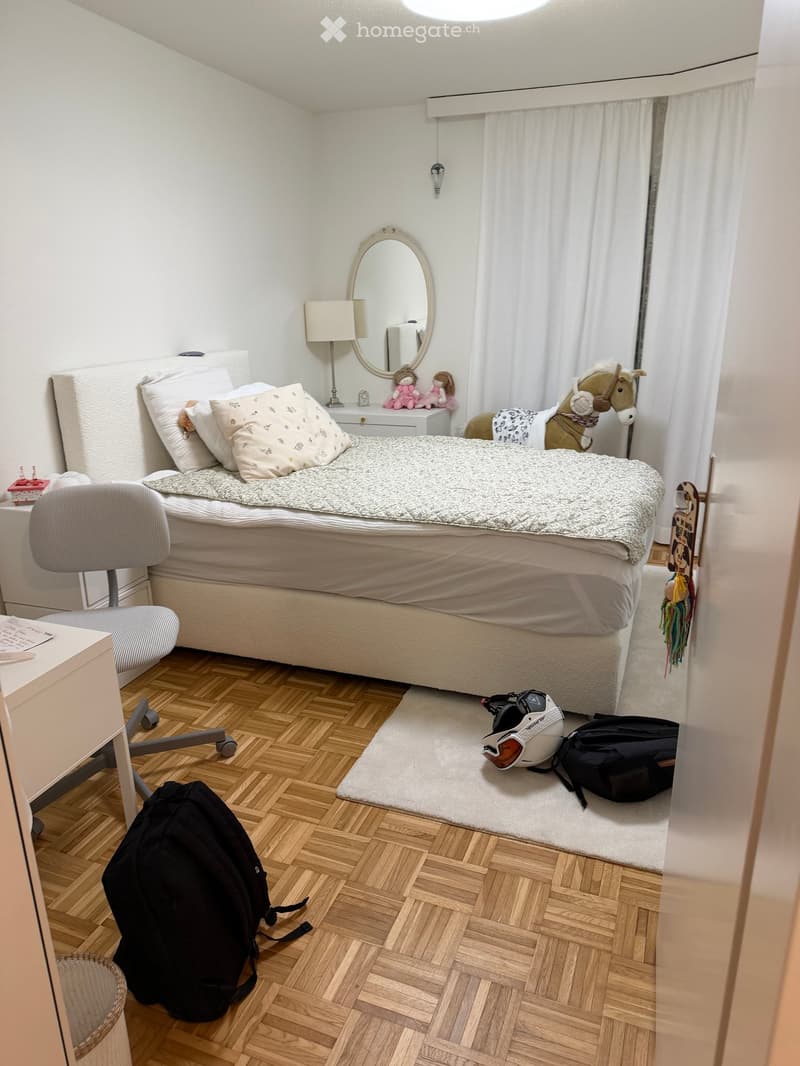 bedroom with a bed, chair, desk, lamp, mirror, toys, and a backpack