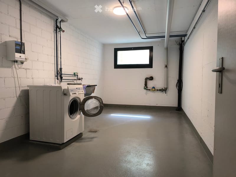 Utility room with a washing machine, exposed brick walls, and a window.