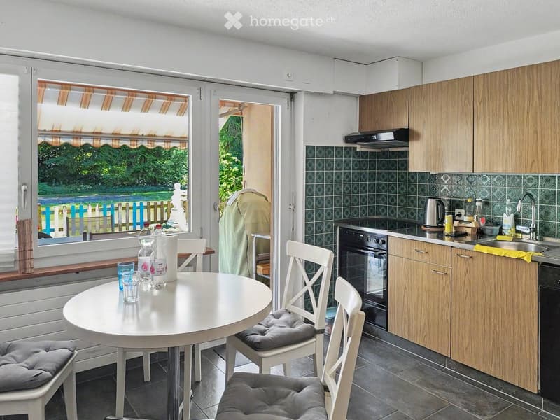 Bright kitchen with wooden cabinets, a round dining table with four chairs, and a window overlooking a garden.