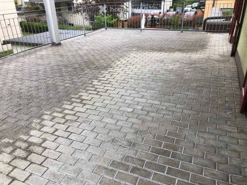 Brick-paved balcony with metal railing, overlooking a residential area with parked cars and greenery.