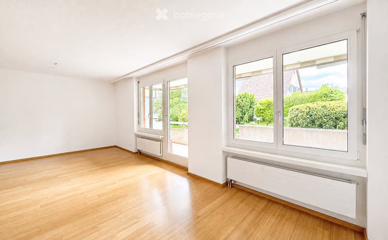 Empty room with wooden flooring, white walls, large windows, and radiators. No furniture or equipment present.
