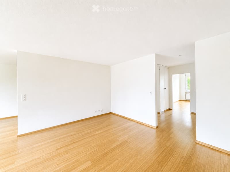 Empty room with light-colored wooden flooring and white walls, featuring a doorway leading to another room.