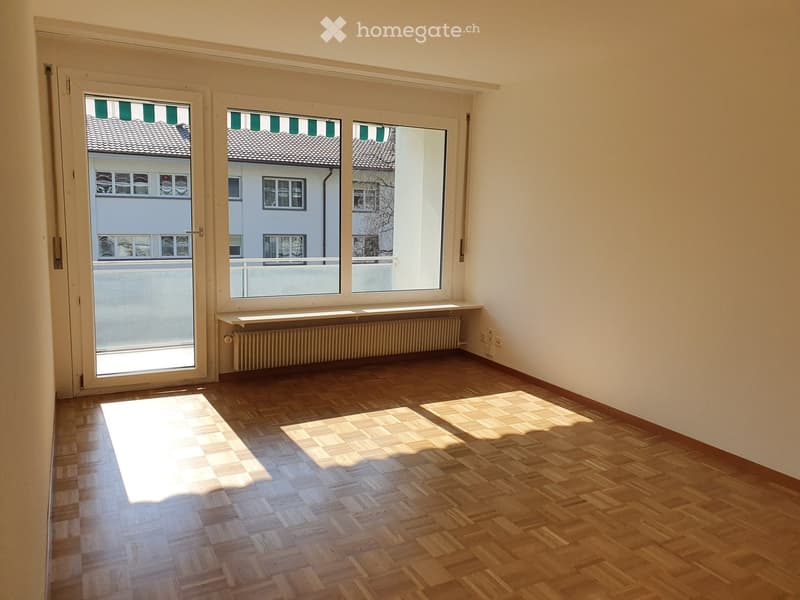 Empty room with wooden flooring, large windows, and a radiator. No furniture or equipment present.