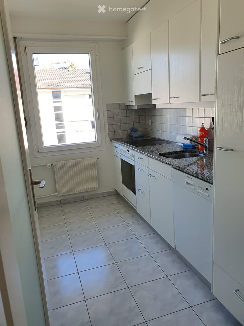 Modern kitchen with white cabinets, granite countertop, sink, oven, dishwasher, and a window overlooking a tiled roof.