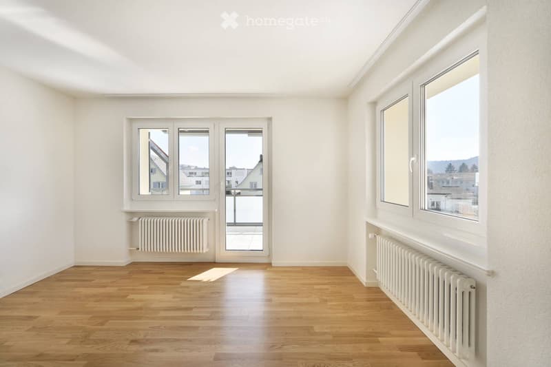 Empty room with wooden flooring, white walls, large windows, and a door leading to a balcony.