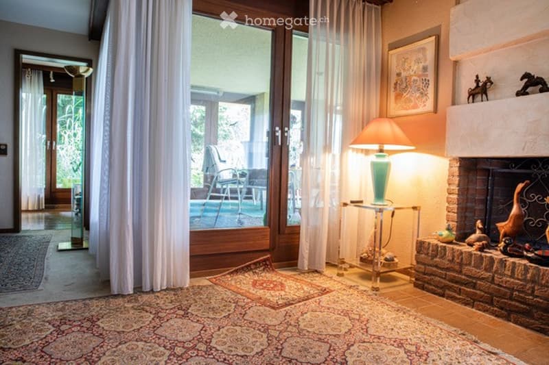 Living room with large windows, fireplace, sofa, coffee table, floor lamp, and a view of a patio with a swimming pool.