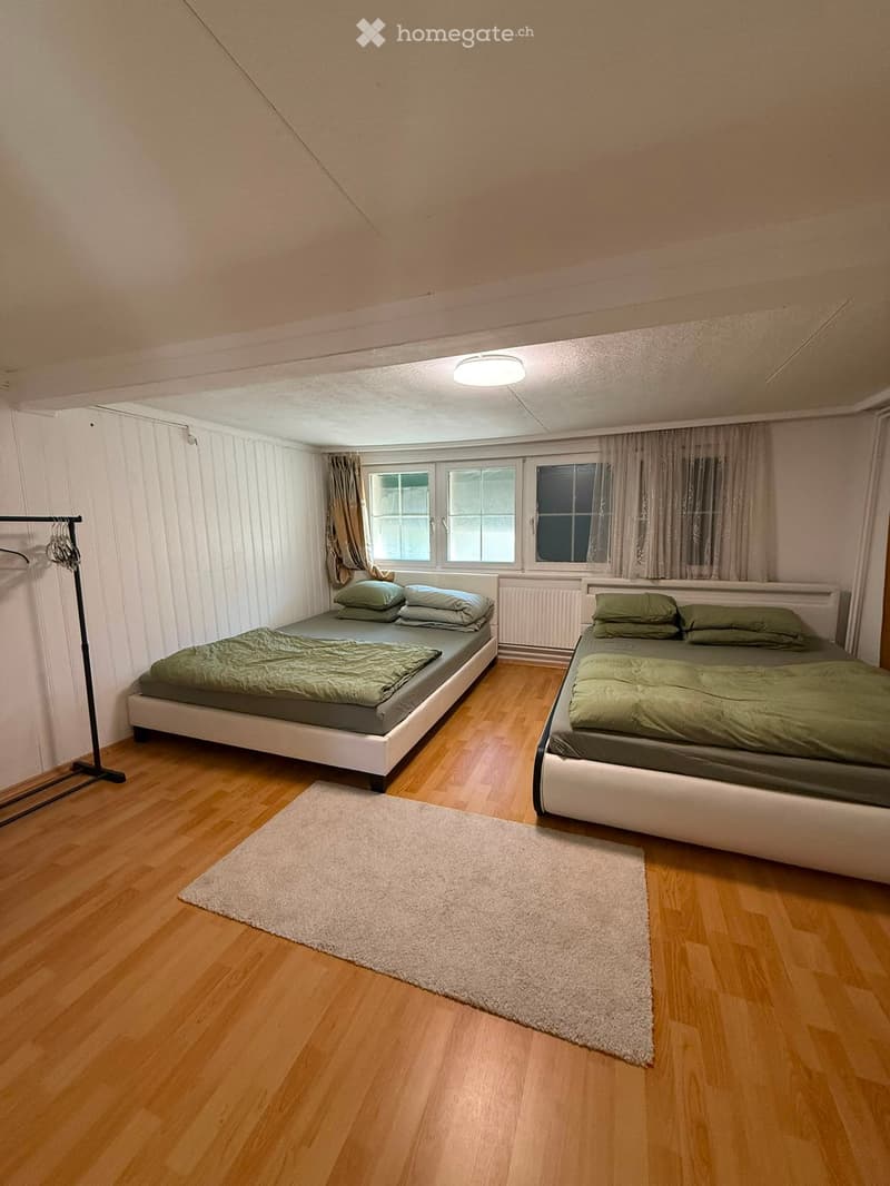 Cozy bedroom with two single beds, green bedding, a white rug, and wooden flooring.