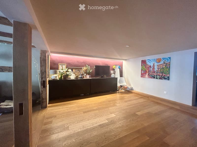 Modern living room with wooden flooring, a dark wooden cabinet, a television, a white chair, and decorative items including vases and artwork.