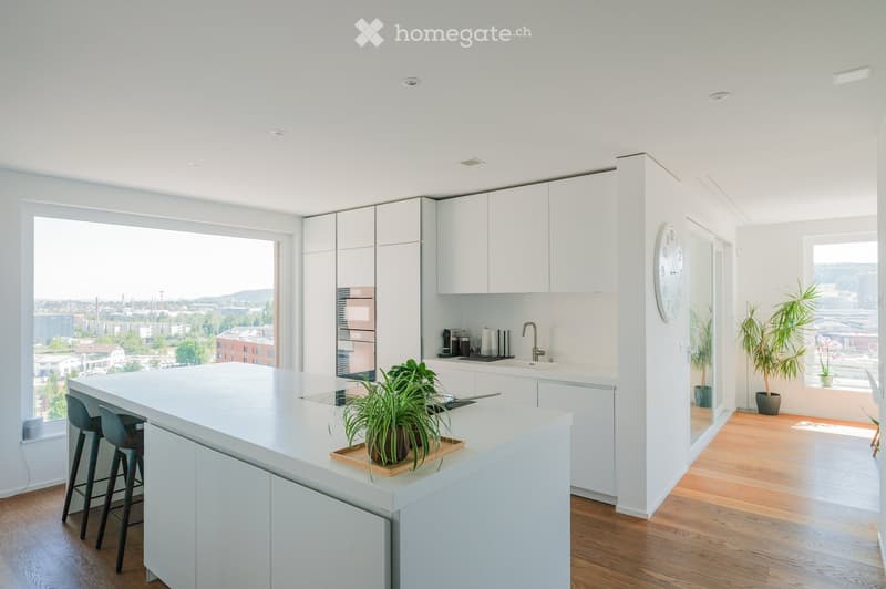 Modern kitchen with white cabinets, a central island, and a large window offering a city view. Includes a sink, faucet, stools, and decorative plants.