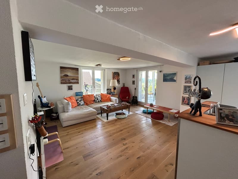 wooden floor, white walls, large glass windows, balcony, large white couch, two side tables, coffee table, floor lamp, chairs, decorative objects