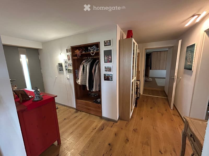 hardwood floor, white walls, large open doorway, clothes hanging, wooden dresser, framed pictures, open closet with clothes and boxes, cabinet with drawers