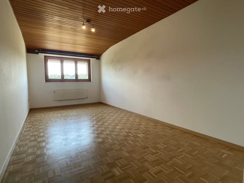 Empty room with wooden parquet flooring, white walls, and a large window with wooden frame. The ceiling is wooden with recessed lighting.