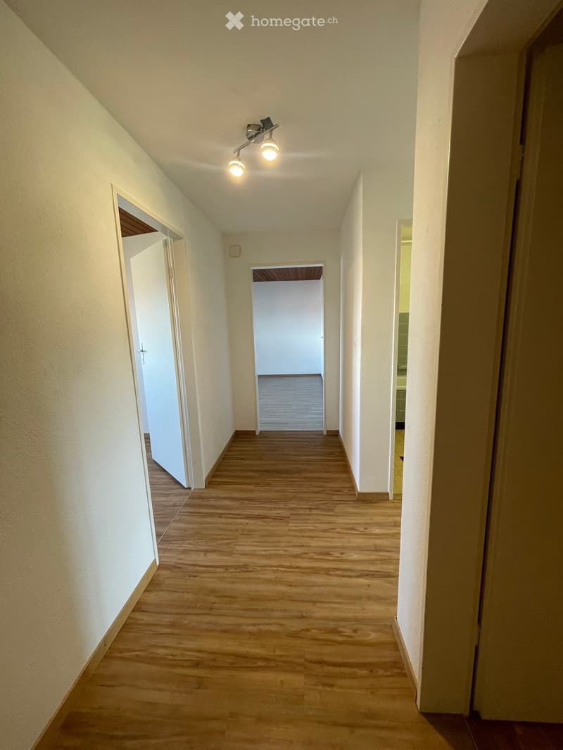 Empty hallway with wooden flooring, white walls, and recessed lighting. Doors lead to adjacent rooms.