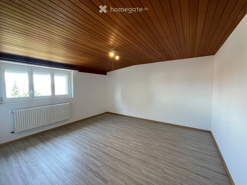 Empty room with wooden flooring, white walls, and a wooden slatted ceiling. Features a window with white frames and a radiator below it.