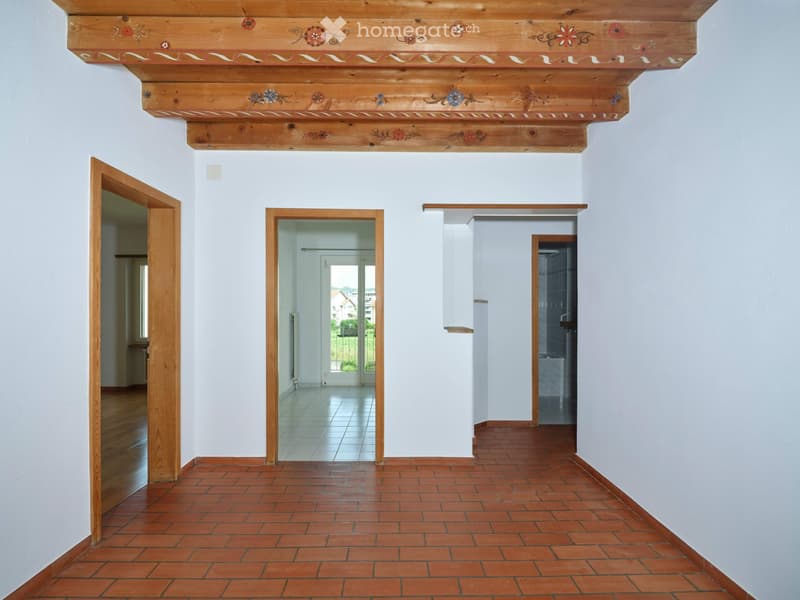 Empty hallway with wooden ceiling, red brick floor, white walls, and several open doors leading to other rooms.