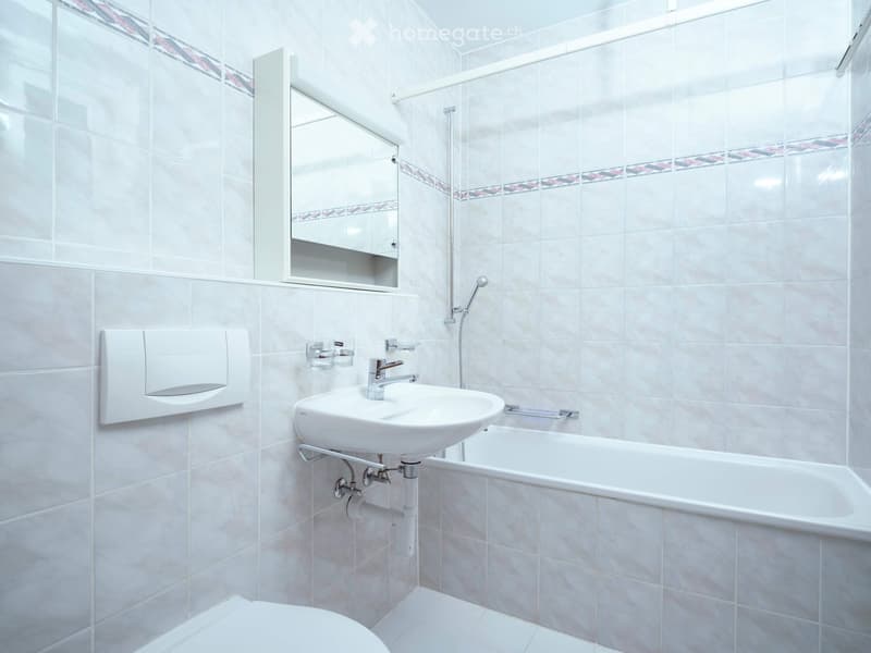 Modern bathroom with white tiles, a sink, bathtub, mirror, and toilet.