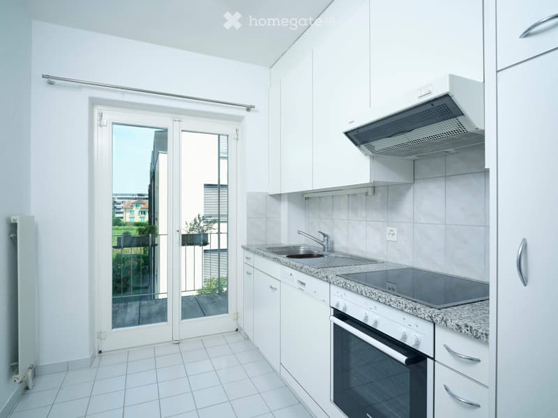 Modern kitchen with white cabinets, granite countertop, stainless steel sink, oven, and range hood. Sliding glass doors lead to a balcony.