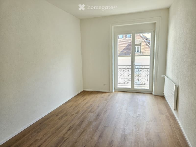 Empty room with wooden flooring, white walls, and a sliding glass door leading to a balcony.
