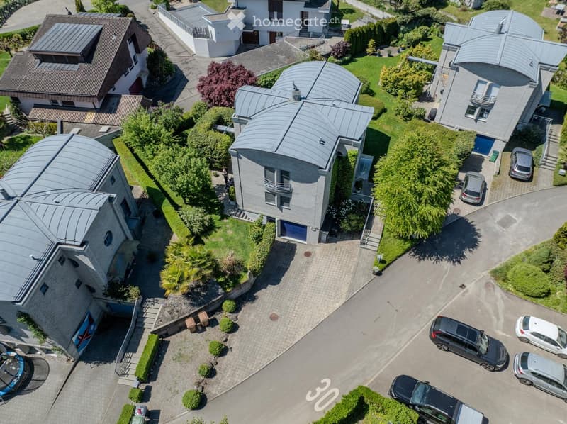 Aerial view of a residential area with multiple modern houses, well-maintained gardens, and parked cars.