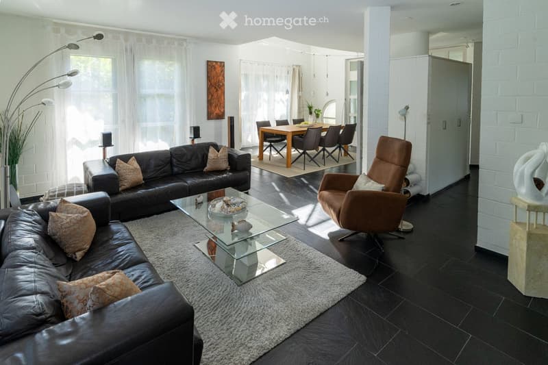 Modern living and dining area with black leather sofa, glass coffee table, dining table with chairs, and decorative items.