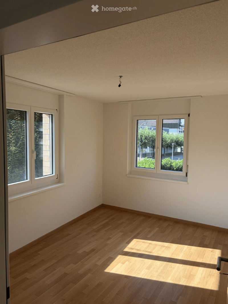 Empty room with wooden flooring, white walls, and multiple windows allowing natural light to enter.
