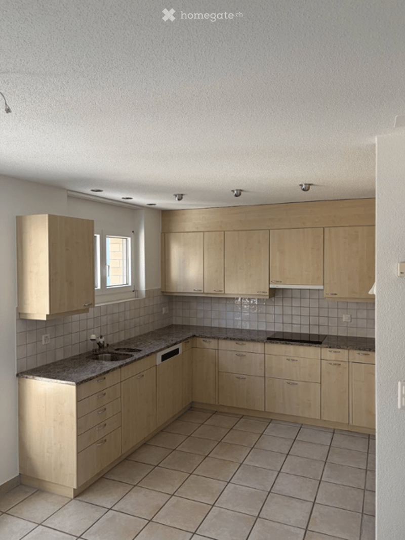 Bright kitchen with light wooden cabinets, granite countertop, and tiled floor. Features a sink with a faucet and built-in storage.