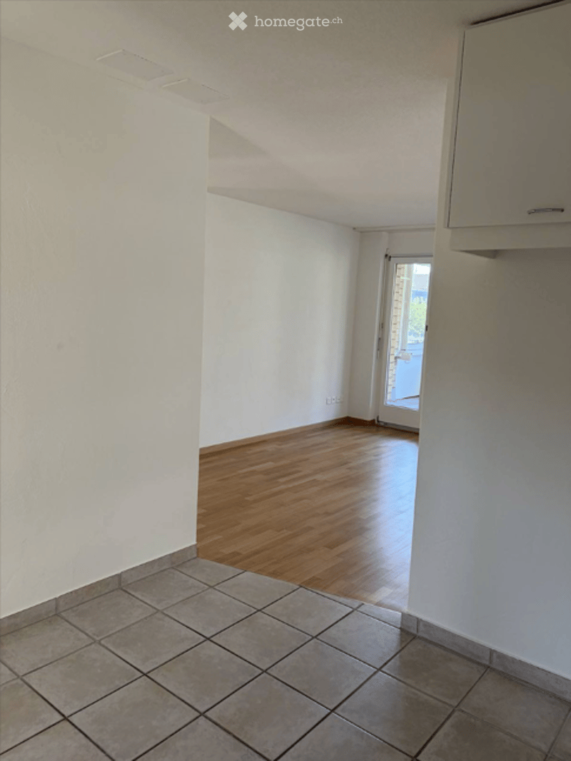 Empty room with white walls, wooden floor, and tiled area near the door. No furniture or equipment visible.
