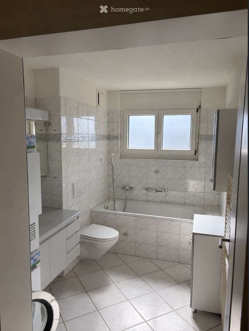 Modern bathroom with white tiles, a bathtub, toilet, sink, and mirrored cabinet.