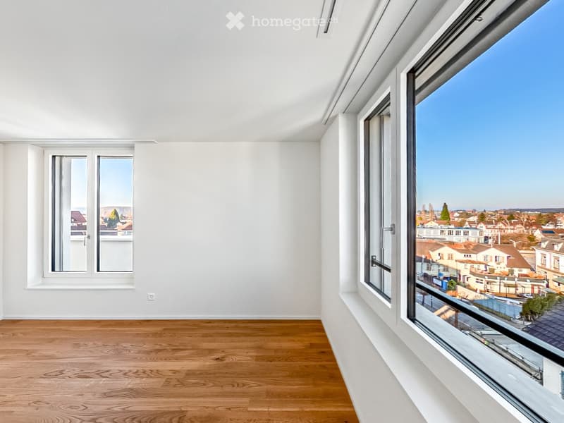 Empty room with wooden flooring, white walls, and large windows offering a view of the cityscape.