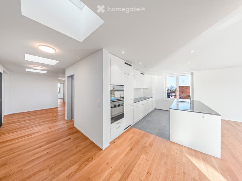 Modern kitchen with white cabinets, stainless steel appliances, wooden flooring, and large windows.