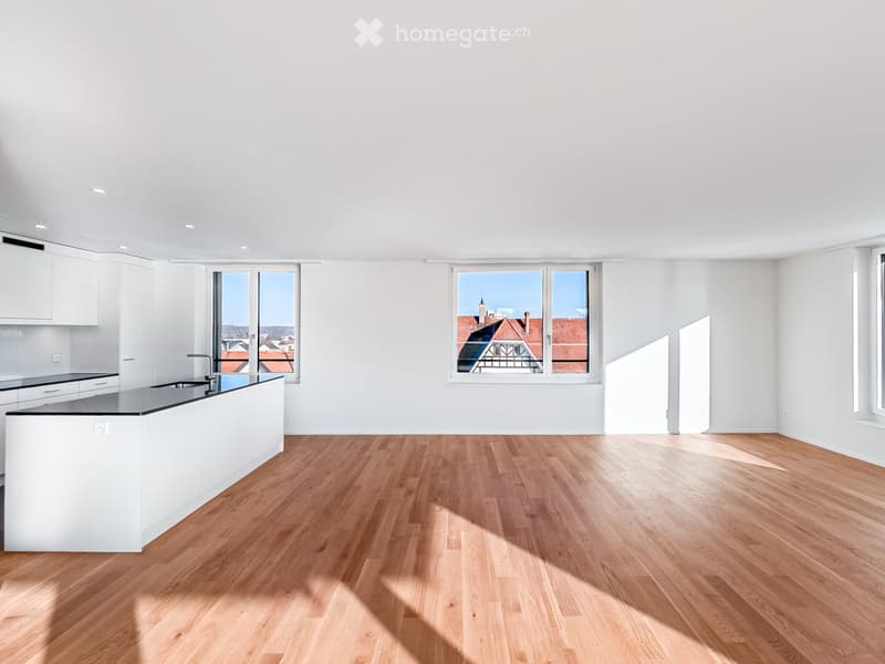 Modern kitchen with white cabinets, a central island, and wooden flooring. Large windows offer a view of the cityscape.