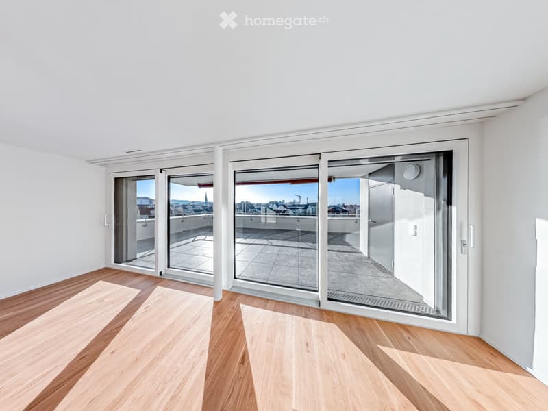 Bright, empty room with light wooden flooring and large sliding glass doors leading to a balcony with city views.