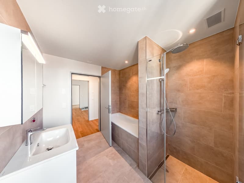 Modern bathroom with a white sink, bathtub, and glass-enclosed shower with a handheld showerhead. Light wood flooring and beige tiles.