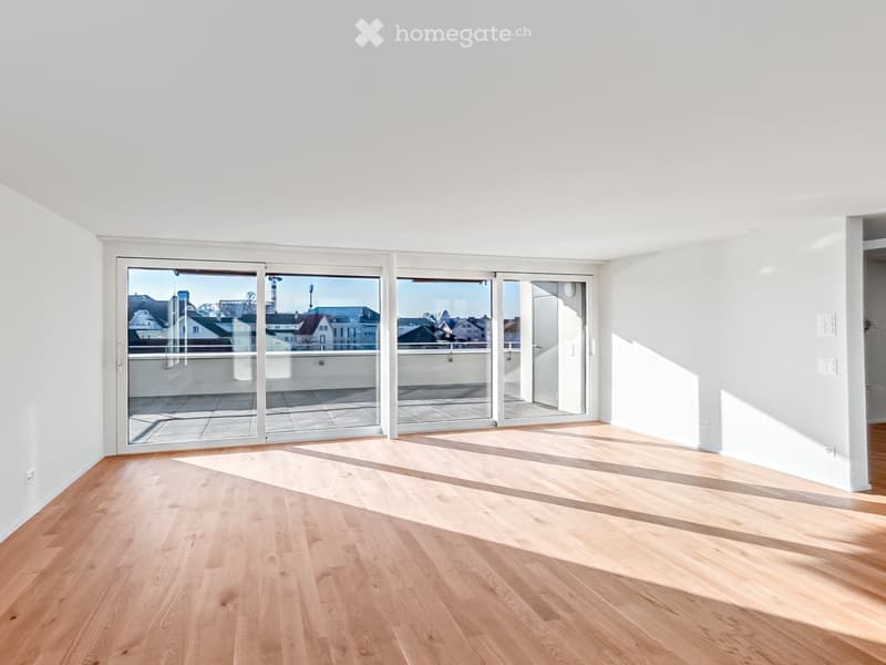 Empty room with light wooden flooring and large glass sliding doors leading to a balcony. The walls are white, and the space is well-lit with natural light.