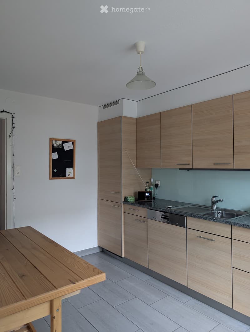 Modern kitchen with light wooden cabinets, a sink, microwave, and a wooden table.