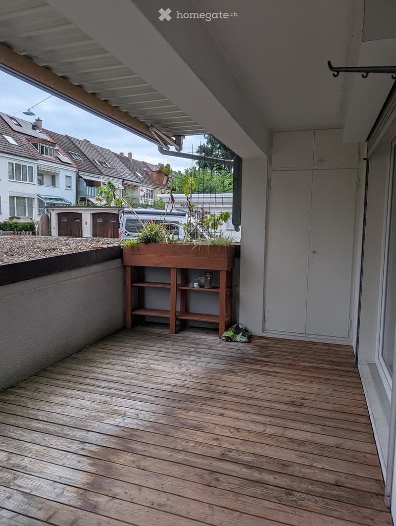 Wooden deck with a small wooden shelf holding a potted plant, overlooking a residential area with houses and parked cars.