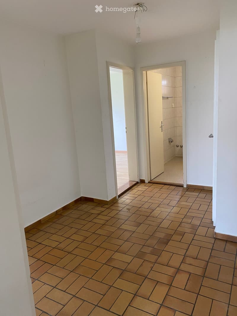 Empty hallway with tiled floor and white walls, featuring two open doors leading to other rooms.