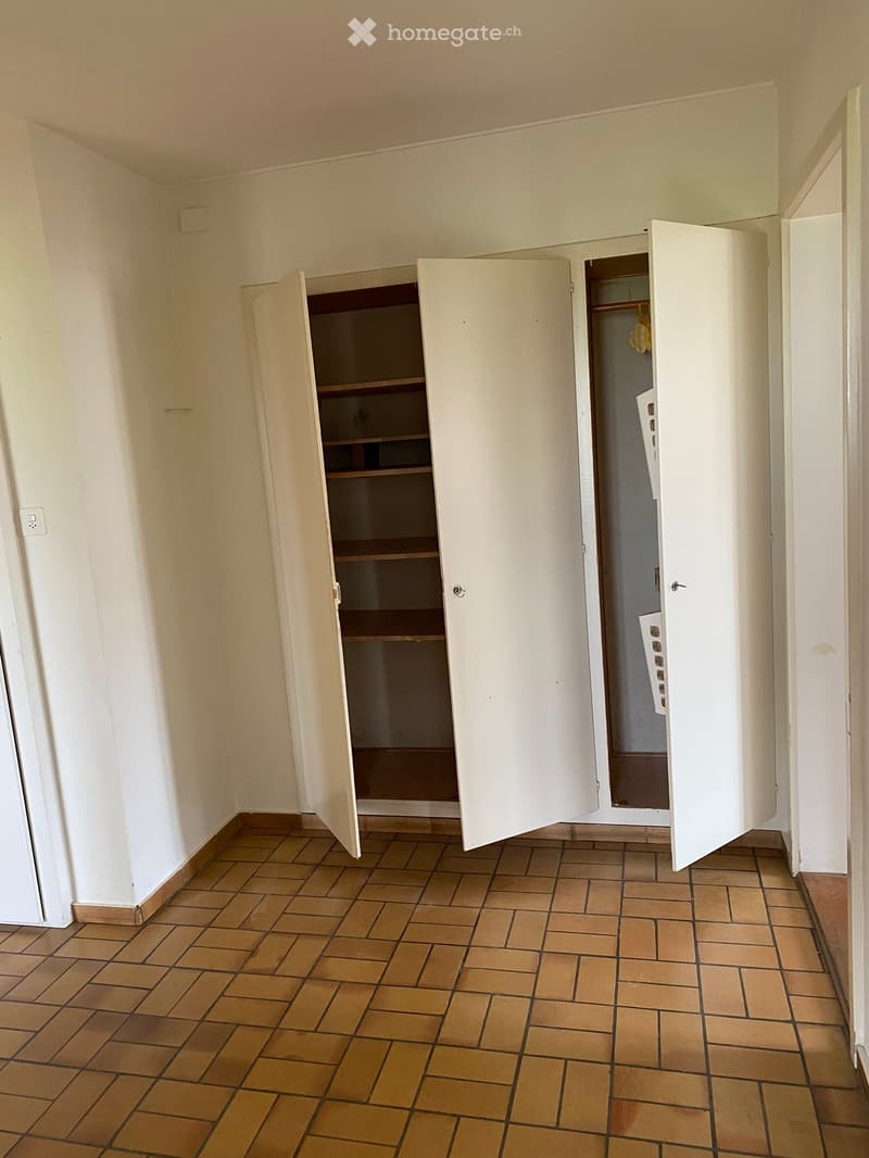 Empty room with tiled floor and white walls, featuring two open built-in wardrobes with empty shelves.