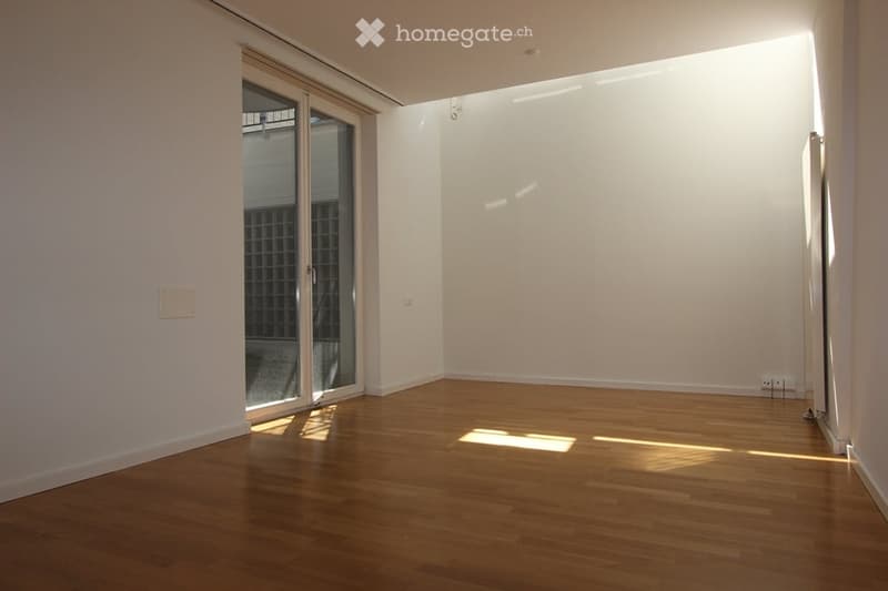 Empty room with wooden flooring, white walls, and a large glass sliding door leading to an outdoor area.