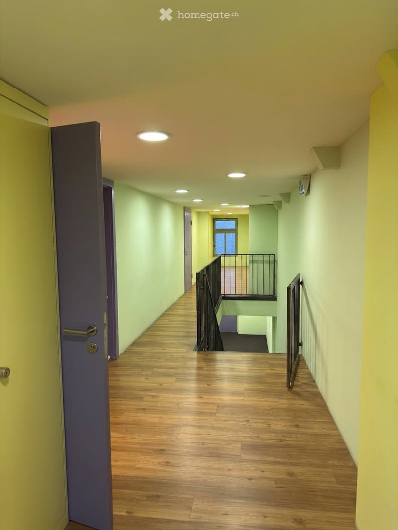 Bright hallway with wooden flooring, recessed ceiling lights, and a staircase leading to an upper level.