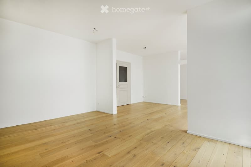 Empty room with white walls and wooden flooring, featuring a white door with a glass panel and visible electrical outlets.