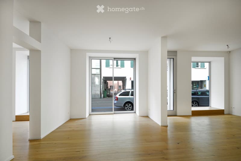 Empty room with wooden flooring, white walls, and large glass doors leading to an outdoor area.