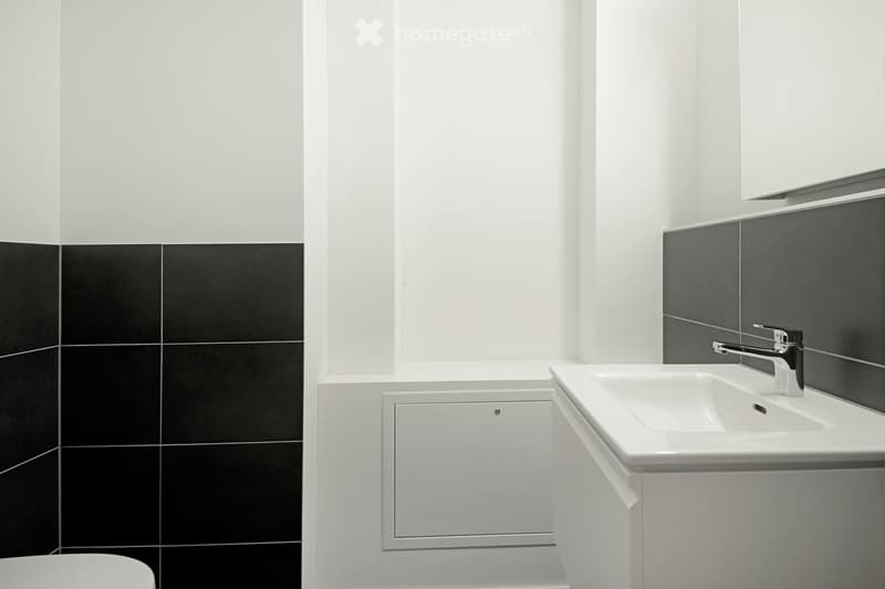 Modern bathroom with white and black tiles, a white sink with a chrome faucet, a toilet, and a mirrored cabinet above the sink.