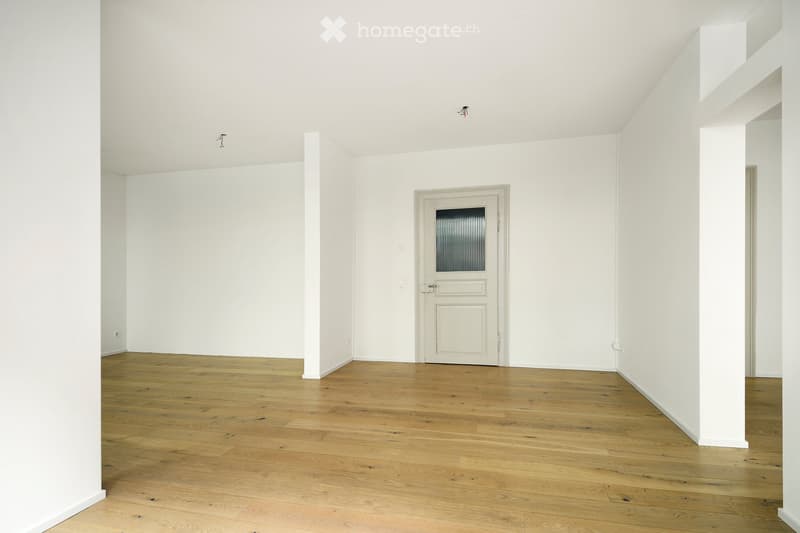 Empty room with white walls, wooden floor, and a single door with a frosted glass panel.